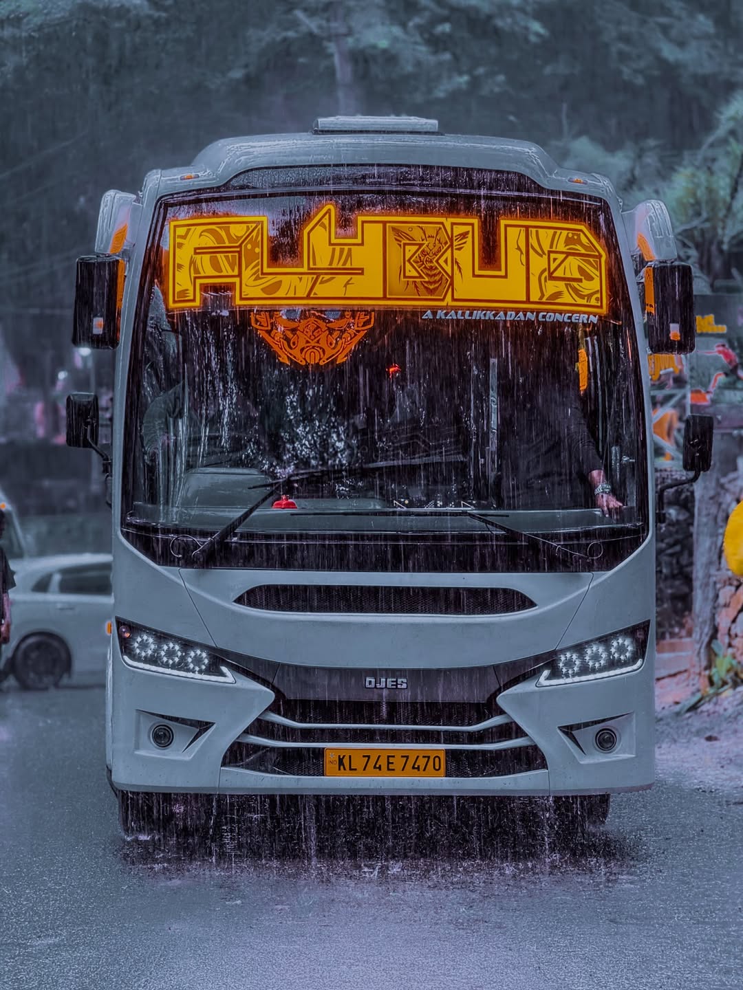A JourneyX touring coach on a wet hill road under heavy monsoon rain.