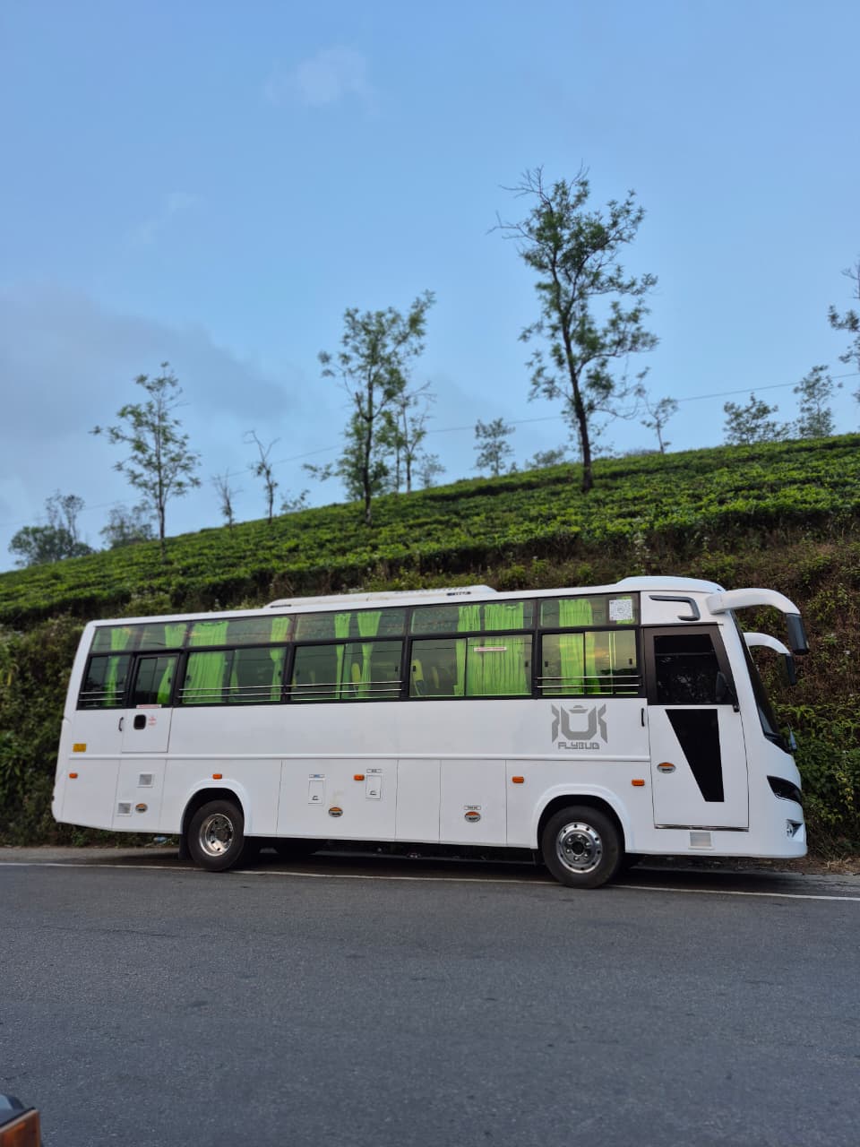 A JourneyX coach with headlights on, moving along a highway in monsoon light.