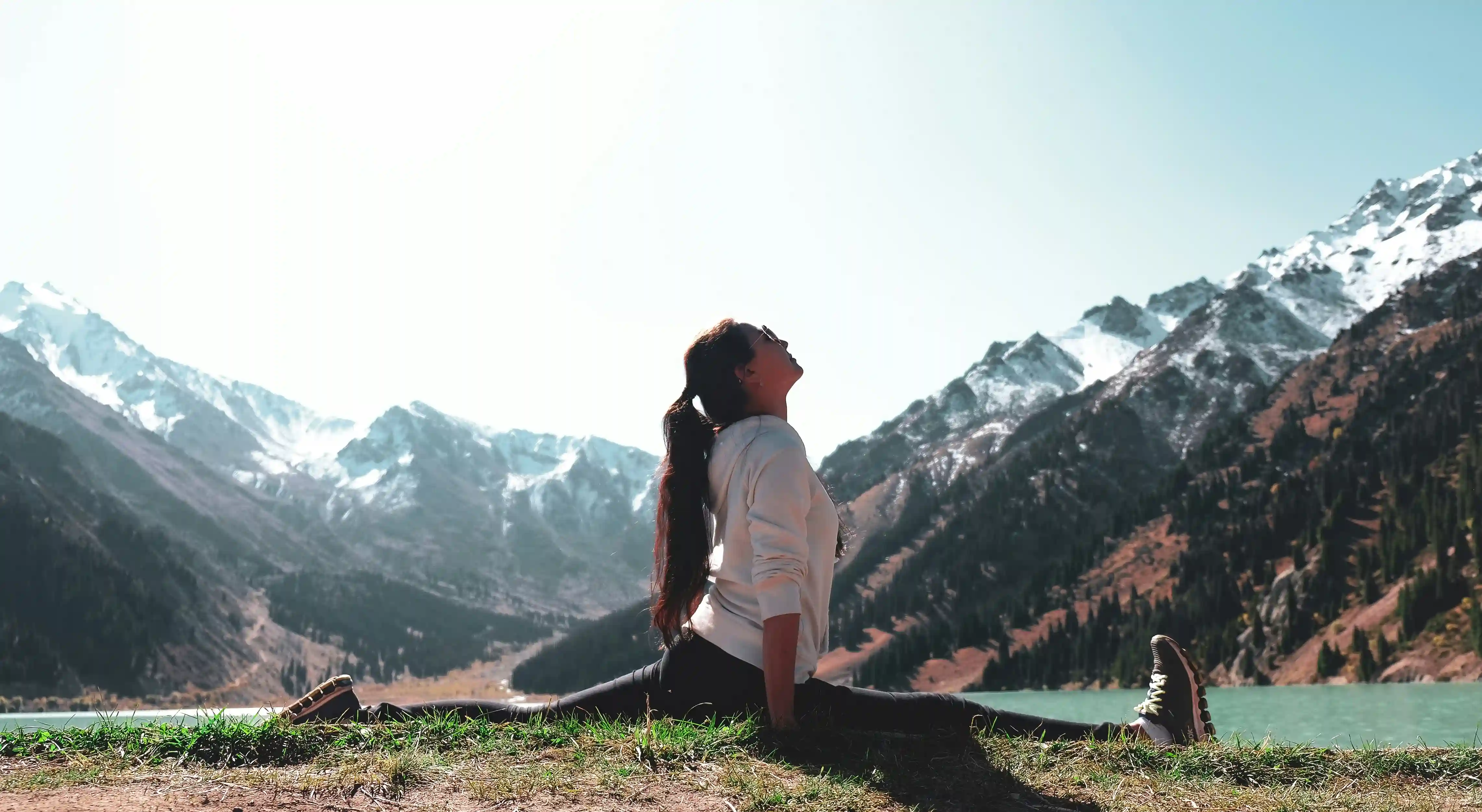 Yogi in Tree Pose by water with mountain backdrop