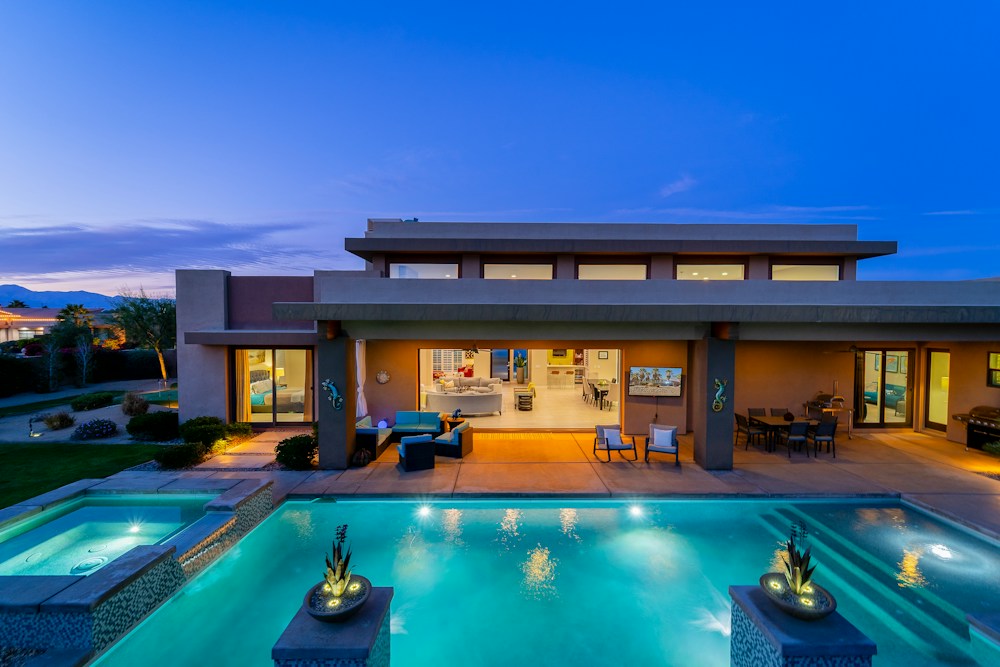 Modern luxury villa with warm interior lighting and an illuminated pool at dusk