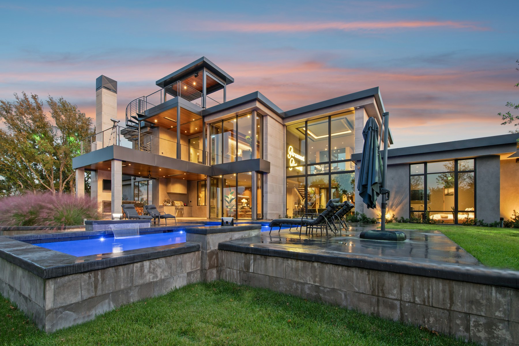 Contemporary luxury residence at dusk with floor-to-ceiling glass, warm interior lighting and landscaped pool terraces