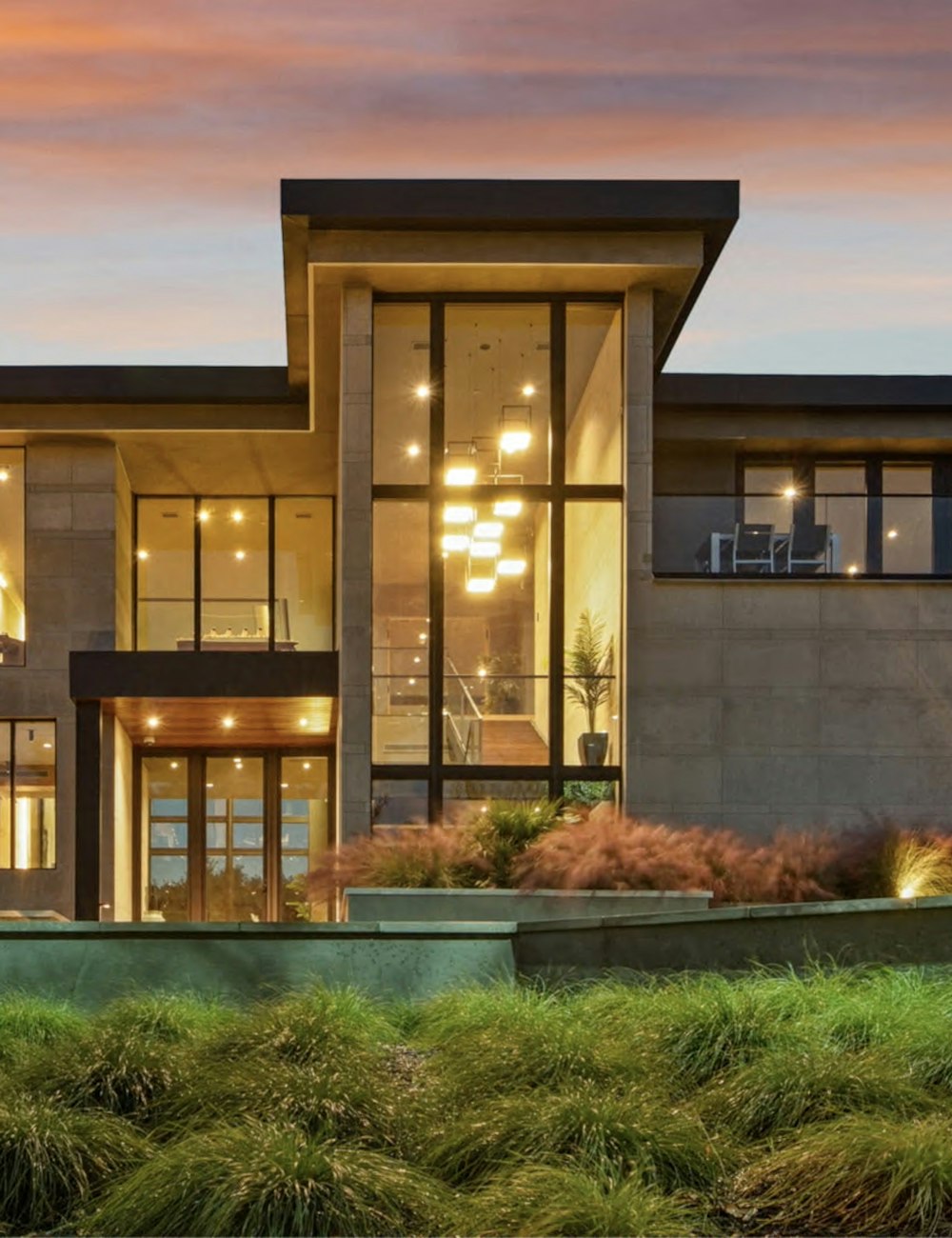 Modern Nexora residence with double-height glass, stone cladding and warm interior lighting at sunset