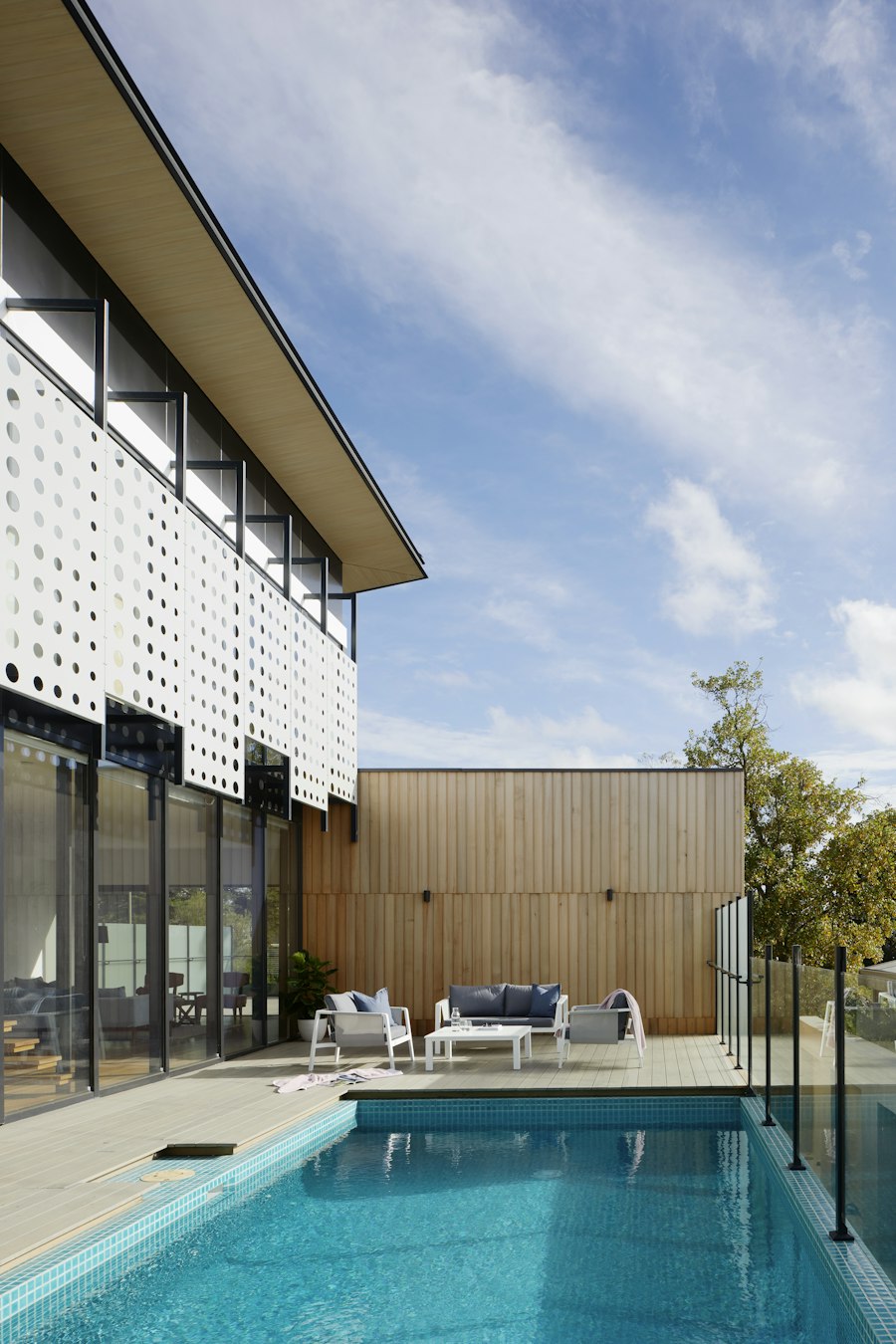 Timber-battened facade with perforated white screens framed by mature trees